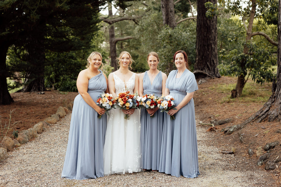 Four women standing outdoors on a gravel path in a wooded setting. Holding colourful faux wedding bouquets. Flowers by Flowers For Ever After