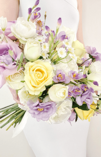 Artificial wedding bridal bouquet held by a bride, with lilac, yellow and white faux roses, white peonies and purple flower spikes. Made in Melbourne by Flowers For Ever After, shipping Australia and Worldwide.