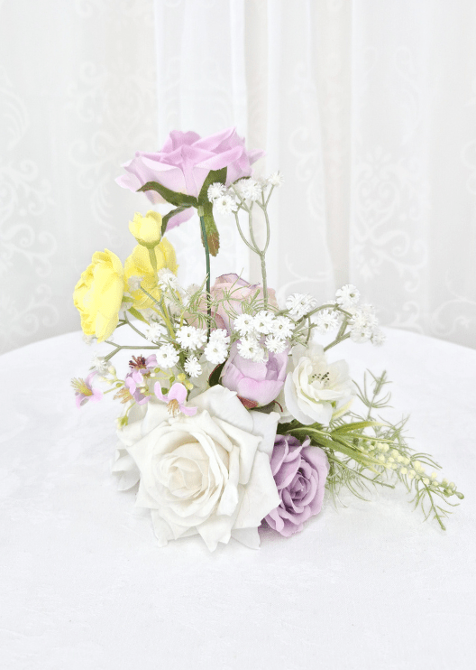 Artificial wedding small table arrangement, reverse view of lilac and white faux roses, yellow blooms and fine white sprigs. Made in Melbourne by Flowers For Ever After, shipping Australia and Worldwide.