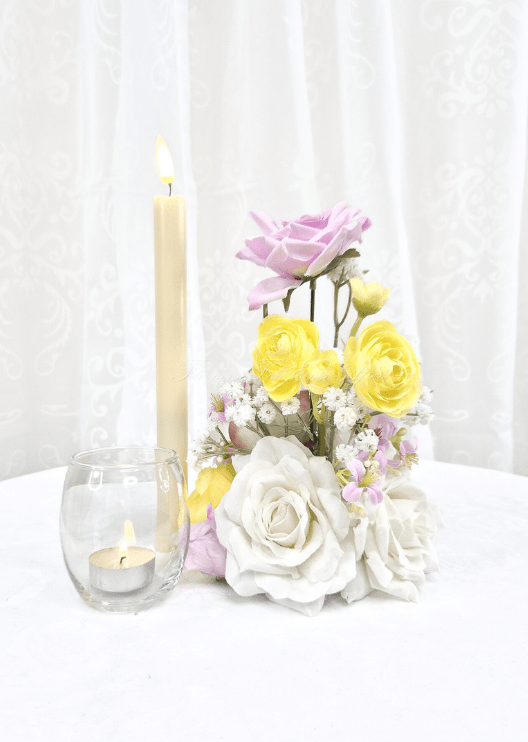 Artificial wedding small table arrangement with lilac, yellow and white faux roses and fine white flower sprigs beside candles. Made in Melbourne by Flowers For Ever After, shipping Australia and Worldwide.