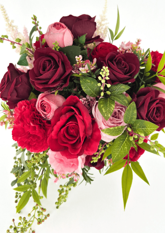 Artificial wedding bridal bouquet, angled view of red, burgundy and pink faux roses, red carnation, variegated green leaves and trailing berry sprigs. Made in Melbourne by Flowers For Ever After, shipping Australia and Worldwide.