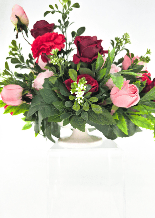 Artificial wedding table arrangement, side view of pink and burgundy faux roses, red carnations and green foliage in a low ivory vessel. Made in Melbourne by Flowers For Ever After, shipping Australia and Worldwide.