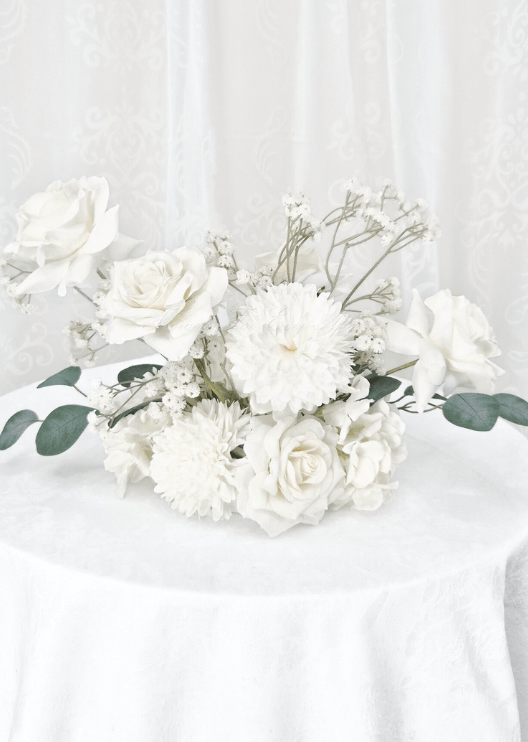 Artificial wedding table centrepiece with white faux roses, white pompom blooms, fine white sprigs and spreading eucalyptus. Made in Melbourne by Flowers For Ever After, shipping Australia and Worldwide.