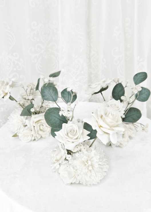 Artificial wedding group of small table arrangements with white faux roses, white pompom blooms and eucalyptus leaves. Made in Melbourne by Flowers For Ever After, shipping Australia and Worldwide.