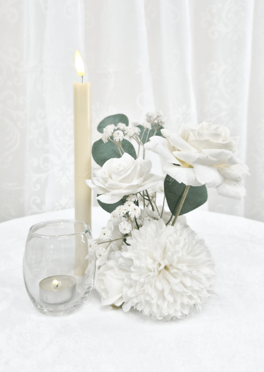 Artificial wedding small table arrangement with white faux roses, white pompom bloom, tiny white sprigs and eucalyptus beside candles. Made in Melbourne by Flowers For Ever After, shipping Australia and Worldwide.