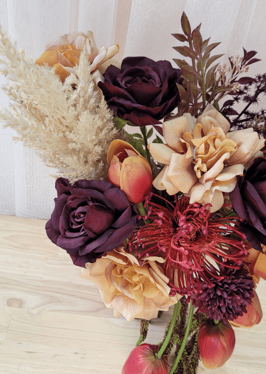 Artificial wedding bouquet detail showing burgundy faux roses, beige blooms, red spiky flower and pale plumes. Made in Melbourne by Flowers For Ever After, shipping Australia and Worldwide.