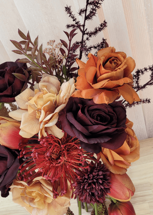 Artificial wedding bouquet close-up with orange and burgundy faux roses, beige blooms, red spiky flower and dark branching sprigs. Made in Melbourne by Flowers For Ever After, shipping Australia and Worldwide.