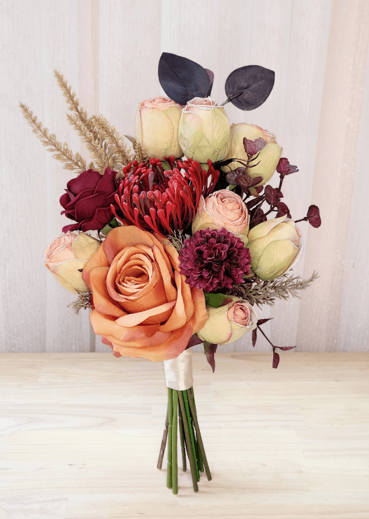 Artificial wedding small bouquet with orange and burgundy faux roses, cream-pink rosebuds, red spiky bloom and dark eucalyptus. Made in Melbourne by Flowers For Ever After, shipping Australia and Worldwide.