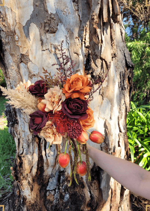 Artificial wedding bouquet held in one hand, close view of orange and burgundy faux roses, beige blooms and trailing tulips. Made in Melbourne by Flowers For Ever After, shipping Australia and Worldwide.