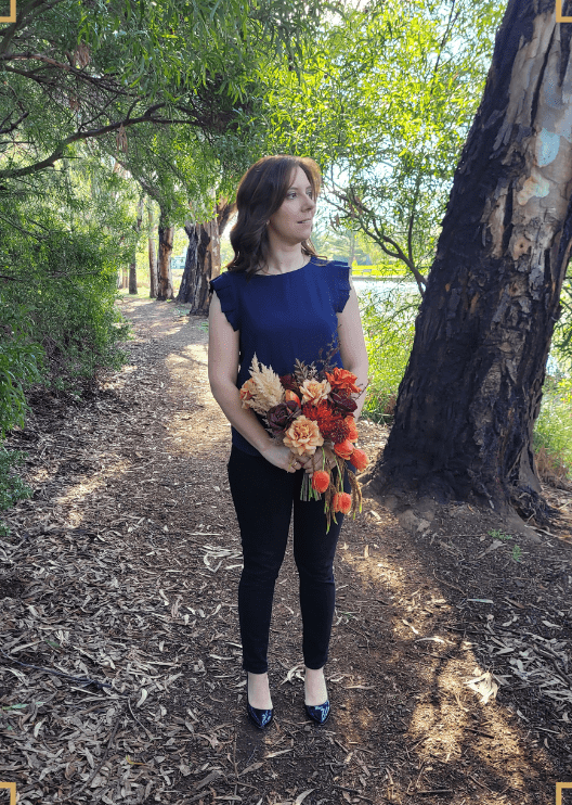 Artificial wedding bouquet held by a person, with orange and burgundy faux roses, beige blooms, pale plumes and trailing tulips. Made in Melbourne by Flowers For Ever After, shipping Australia and Worldwide.