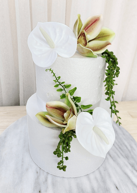 Artificial wedding cake decoration, angled view of white faux anthuriums, green-and-burgundy orchids and trailing green leaves. For birthday, event and celebration cakes. Made in Melbourne by Flowers For Ever After, shipping Australia and Worldwide.