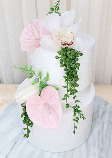 Artificial wedding cake decoration, angled view of pale pink faux anthuriums, white speckled orchid and trailing green strands. For birthday, event and celebration cakes. Made in Melbourne by Flowers For Ever After, shipping Australia and Worldwide.