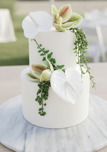 Artificial wedding cake decoration with white faux anthuriums, green-and-burgundy orchids and trailing green leaves across two tiers. For birthday, event and celebration cakes. Made in Melbourne by Flowers For Ever After, shipping Australia and Worldwide.