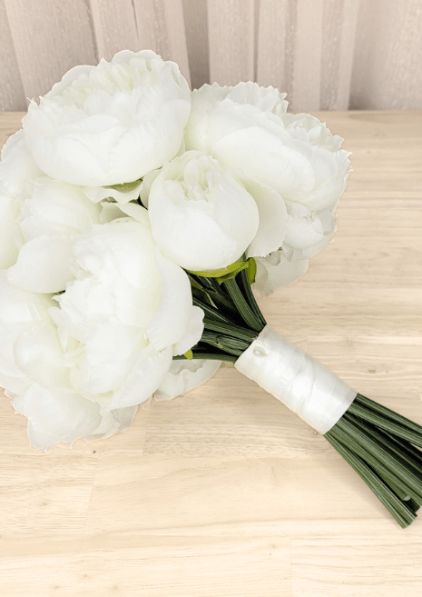 Artificial wedding bridesmaid bouquet laid sideways, showing white faux peonies, gathered green stems and white ribbon wrapping. Made in Melbourne by Flowers For Ever After, shipping Australia and Worldwide.
