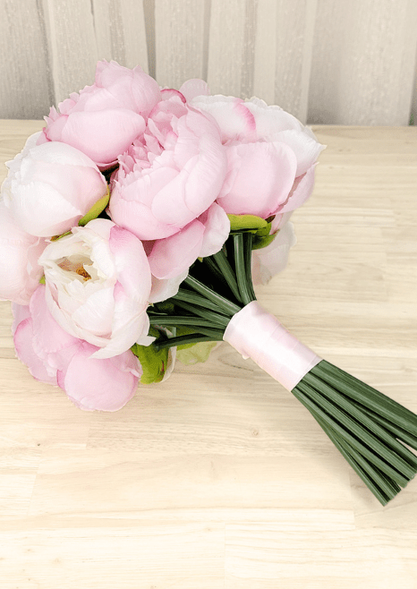 Artificial wedding bridesmaid bouquet laid sideways, showing pink and ivory faux peonies and pink-wrapped green stems. Made in Melbourne by Flowers For Ever After, shipping Australia and Worldwide.