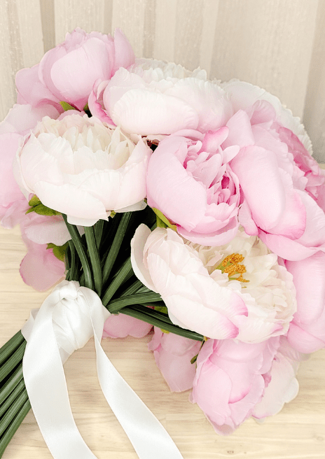 Artificial wedding bouquet laid sideways, showing pink and ivory faux peonies, gathered green stems and white ribbon tails. Made in Melbourne by Flowers For Ever After, shipping Australia and Worldwide.