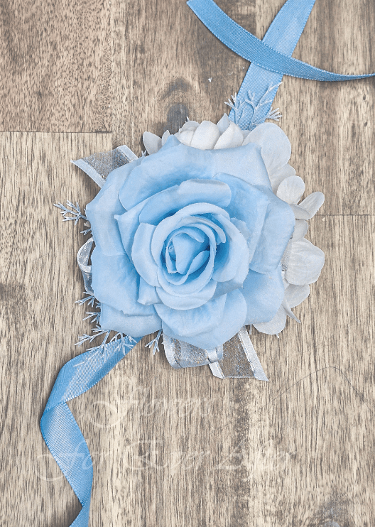 Artificial wedding wrist corsage, angled view of light blue faux roses, white filler flowers and trailing ivory ribbons. For formals, proms and ball occasions. Made in Melbourne by Flowers For Ever After, shipping Australia and Worldwide.