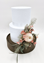 Artificial wedding cake decoration with faux banksia blooms and mixed native-style foliage arranged over cake tiers. For birthday, event and celebration cakes. Made in Melbourne by Flowers For Ever After, shipping Australia and Worldwide.