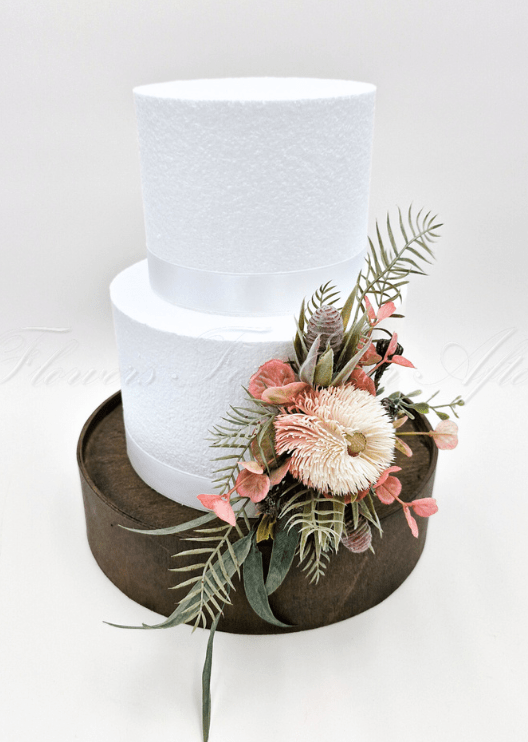 Artificial wedding cake decoration with faux banksia blooms and mixed native-style foliage arranged over cake tiers. For birthday, event and celebration cakes. Made in Melbourne by Flowers For Ever After, shipping Australia and Worldwide.