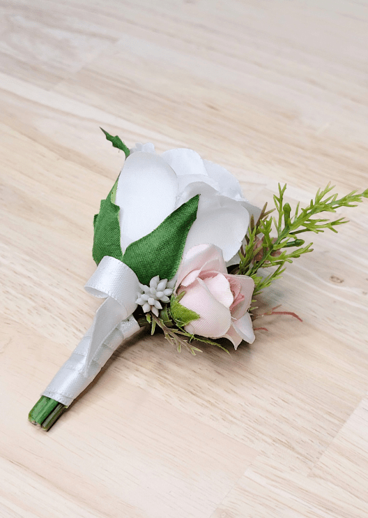 Artificial wedding boutonniere, angled view of a white faux rose, pale blush rosebud, tiny white flowers and fine greenery. For formals, proms and ball occasions. Made in Melbourne by Flowers For Ever After, shipping Australia and Worldwide.