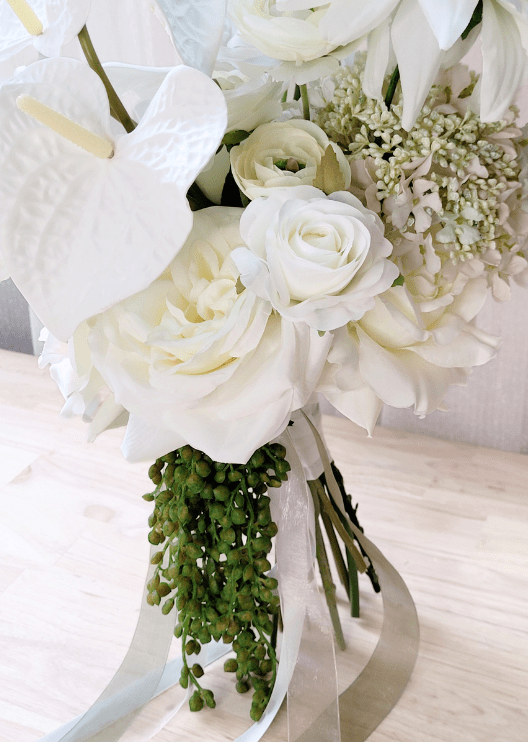 Artificial wedding bouquet detail showing white faux roses, ranunculus, anthurium and trailing green berries beside white and grey ribbons. Made in Melbourne by Flowers For Ever After, shipping Australia and Worldwide.