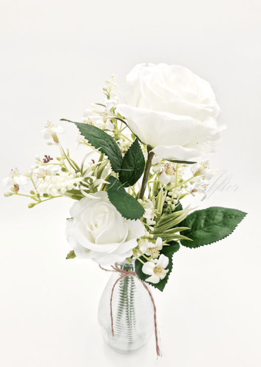 Artificial wedding table arrangement, angled view of white faux roses, tiny cream flowers and green leaves in a ribbed glass bottle. Made in Melbourne by Flowers For Ever After, shipping Australia and Worldwide.