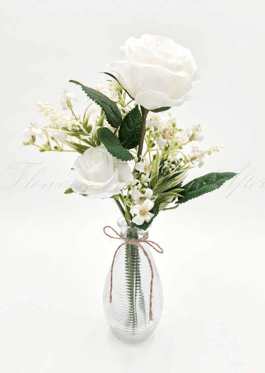 Artificial wedding table arrangement with white faux roses, tiny cream flowers and green leaves in a twine-tied ribbed glass bottle. Made in Melbourne by Flowers For Ever After, shipping Australia and Worldwide.