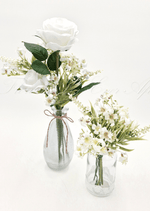 Artificial wedding table flower pair with white faux roses in a twine-tied ribbed bottle and small cream flowers in a glass jar. Made in Melbourne by Flowers For Ever After, shipping Australia and Worldwide.