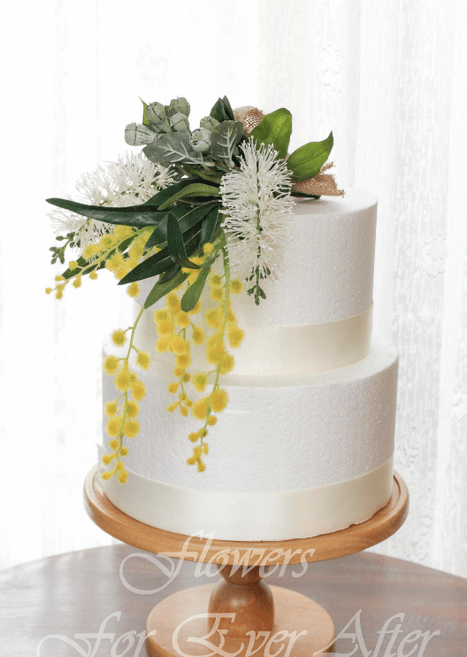 Artificial wedding cake decoration with red faux bottlebrush flowers, yellow wattle clusters and grey-green leaves arranged over three tiers. For birthday, event and celebration cakes. Made in Melbourne by Flowers For Ever After, shipping Australia and Worldwide.