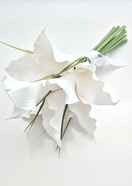 Artificial wedding calla lily bouquet, angled view of white faux blooms, long green leaves and stems tied with a white bow. Made in Melbourne by Flowers For Ever After, shipping Australia and Worldwide.