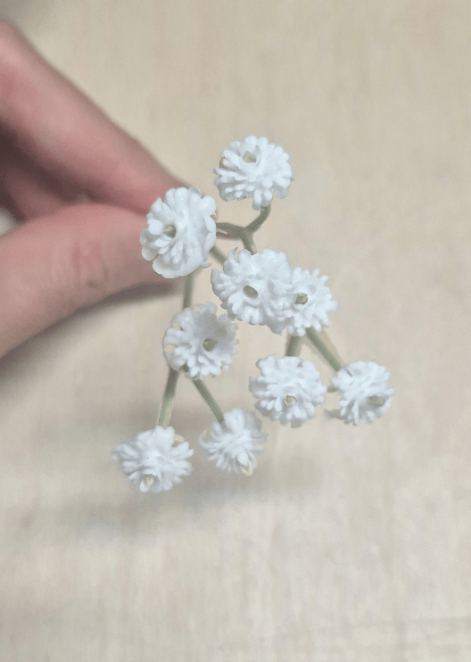 Artificial wedding flower close-up showing a hand holding a sprig of tiny white faux baby's breath blooms. Made in Melbourne by Flowers For Ever After, shipping Australia and Worldwide.