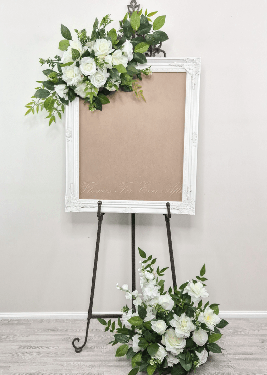 Artificial wedding sign floral set with white faux roses and green foliage above the frame and in a floor arrangement. Made in Melbourne by Flowers For Ever After, shipping Australia and Worldwide.
