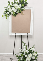 Artificial wedding sign floral set with white faux roses and green foliage above the frame and in a floor arrangement. Made in Melbourne by Flowers For Ever After, shipping Australia and Worldwide.