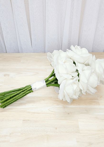 Artificial wedding bouquet laid sideways, showing white-ivory faux roses, green sepals and white-wrapped stems. Made in Melbourne by Flowers For Ever After, shipping Australia and Worldwide.