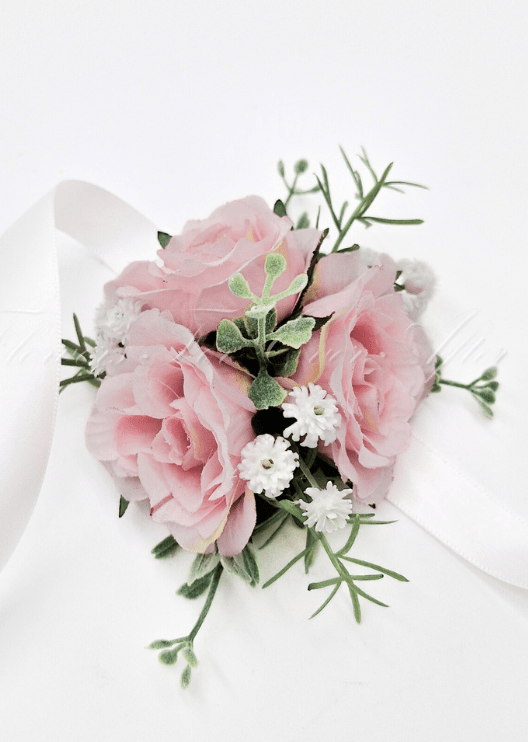 Artificial wedding wrist corsage, angled view of pale pink faux roses, small white flowers and green sprigs with ivory ribbons. For formals, proms and ball occasions. Made in Melbourne by Flowers For Ever After, shipping Australia and Worldwide.