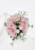 Artificial wedding wrist corsage, angled view of pale pink faux roses, small white flowers and green sprigs with ivory ribbons. For formals, proms and ball occasions. Made in Melbourne by Flowers For Ever After, shipping Australia and Worldwide.
