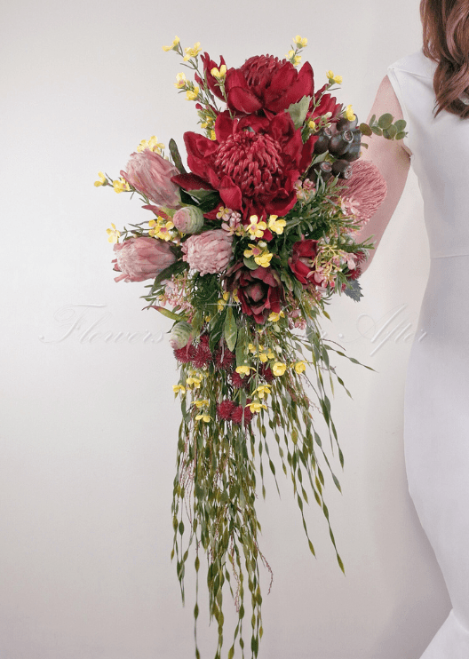 Artificial wedding cascading bridal bouquet, angled view of red faux waratah, pink protea, yellow flowers and long trailing greenery. Made in Melbourne by Flowers For Ever After, shipping Australia and Worldwide.