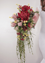 Artificial wedding cascading bridal bouquet, angled view of red faux waratah, pink protea, yellow flowers and long trailing greenery. Made in Melbourne by Flowers For Ever After, shipping Australia and Worldwide.