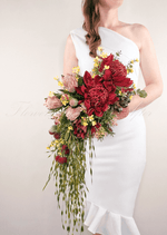 Artificial wedding cascading bridal bouquet held by a bride, with red faux waratah, pink protea, yellow flowers and long trailing foliage. Made in Melbourne by Flowers For Ever After, shipping Australia and Worldwide.