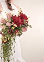 Artificial wedding cascading bridal bouquet held by a bride, with red faux waratah, pink protea, yellow flowers and grey-green foliage. Made in Melbourne by Flowers For Ever After, shipping Australia and Worldwide.