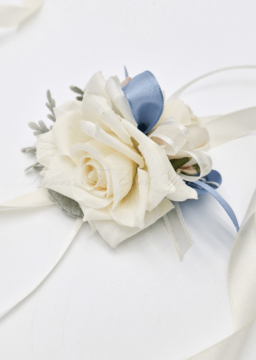 Artificial wedding wrist corsage close-up with cream faux roses, dusty blue ribbon loops and trailing ivory ribbons. For formals, proms and ball occasions. Made in Melbourne by Flowers For Ever After, shipping Australia and Worldwide.