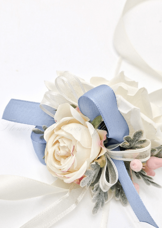 Artificial wedding wrist corsage detail with cream faux rose petals, dusty blue ribbon loops, pink berries and ivory ribbons. For formals, proms and ball occasions. Made in Melbourne by Flowers For Ever After, shipping Australia and Worldwide.