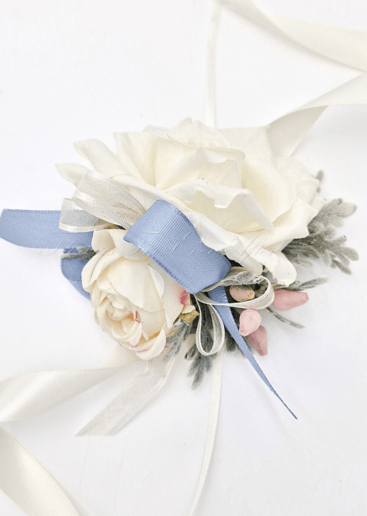 Artificial wedding wrist corsage with cream faux roses, dusty blue ribbon loops, pink berry sprigs and trailing ivory ribbons. For formals, proms and ball occasions. Made in Melbourne by Flowers For Ever After, shipping Australia and Worldwide.