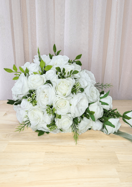 Artificial wedding bouquet laid sideways, showing white faux roses and peonies, tiny buds and trailing green foliage. Made in Melbourne by Flowers For Ever After, shipping Australia and Worldwide.