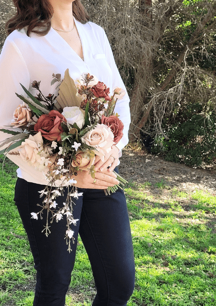 Artificial wedding bouquet held by a person, with terracotta and beige faux roses, pointed leaves and trailing white blossoms. Made in Melbourne by Flowers For Ever After, shipping Australia and Worldwide.