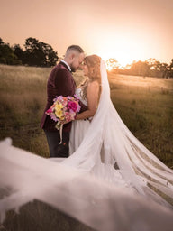 A bride in a white wedding gown with a long veil and a bouquet of artificial pink and yellow flowers. Flowers by Flowers For Ever After