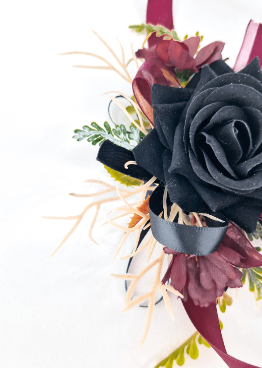 Artificial wedding wrist corsage close-up with a black faux rose, burgundy flowers and black and burgundy ribbon loops. For formals, proms and ball occasions. Made in Melbourne by Flowers For Ever After, shipping Australia and Worldwide.