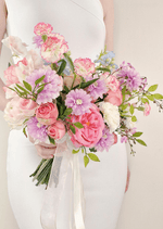 Artificial wedding bridal bouquet held by a bride, with pink faux roses, lilac daisies, white flowers and trailing ivory ribbons. Made in Melbourne by Flowers For Ever After, shipping Australia and Worldwide.