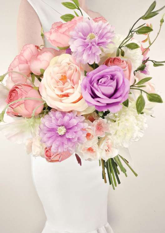 Artificial wedding bridesmaid bouquet close-up with purple and pink faux roses, lilac daisies, white flowers and green foliage. Made in Melbourne by Flowers For Ever After, shipping Australia and Worldwide.