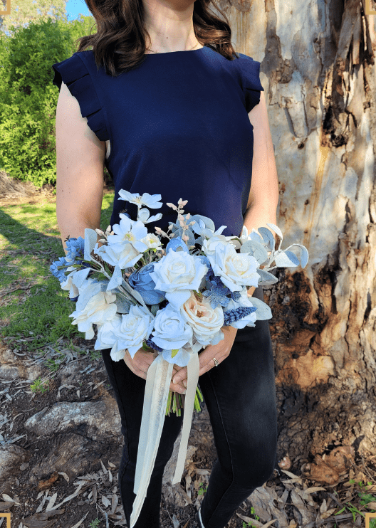 Artificial wedding bridal bouquet held by a bride, with mixed faux blooms, greenery and trailing ribbon. Made in Melbourne by Flowers For Ever After, shipping Australia and Worldwide.